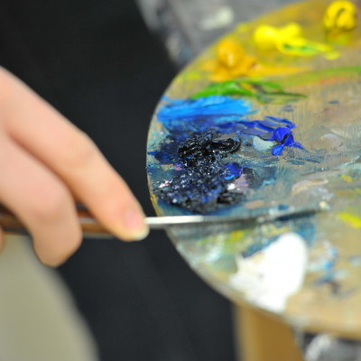 Close up of a student's hand painting and holding a paint palette
