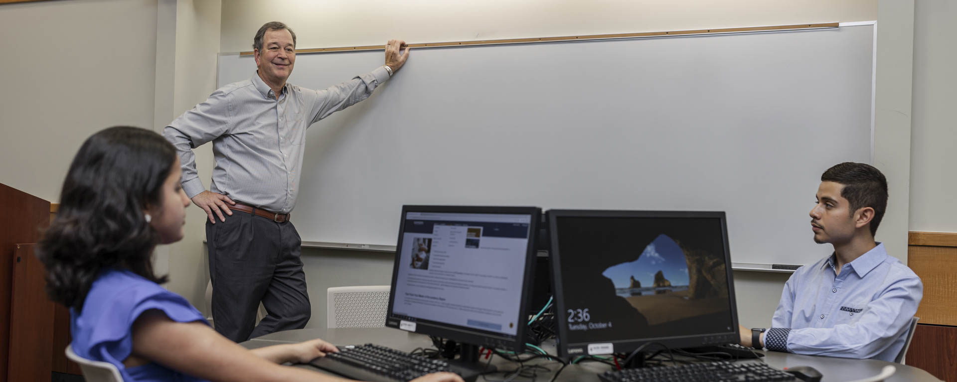 A business professor stands at a white board while talking with students.
