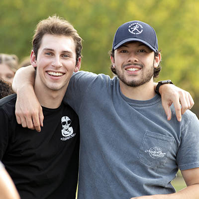 Two Washburn students smile while one has their arm wrapped around the other's shoulder.
