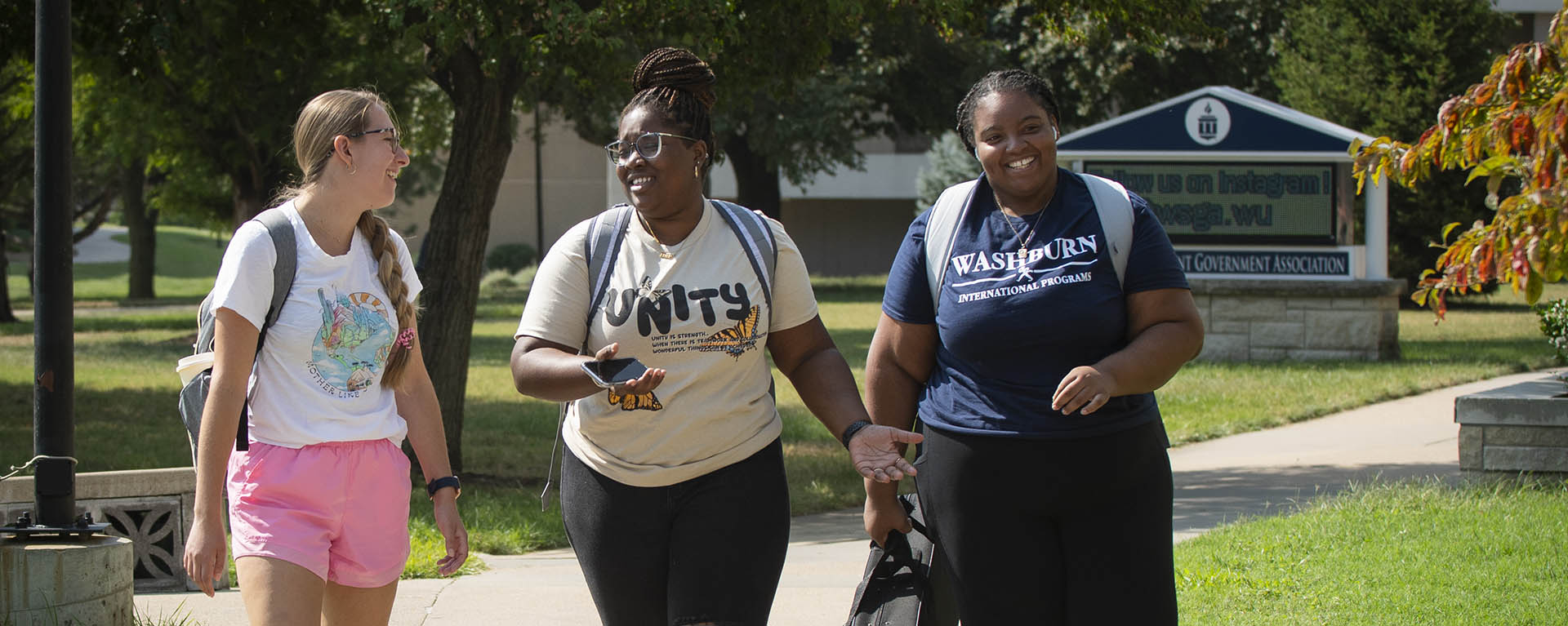 Three Washburn students smile and chat while walking to class on campus.
