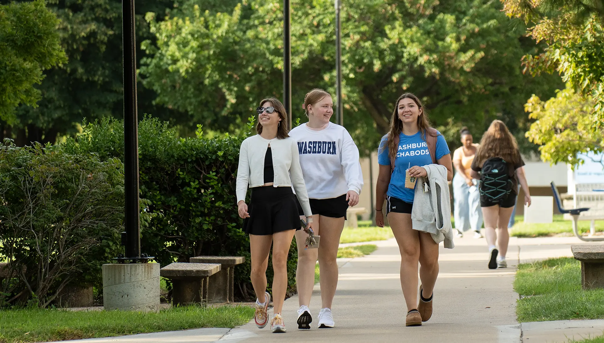 Three students wearing Washburn shirts smile as they walk to class on the first day.