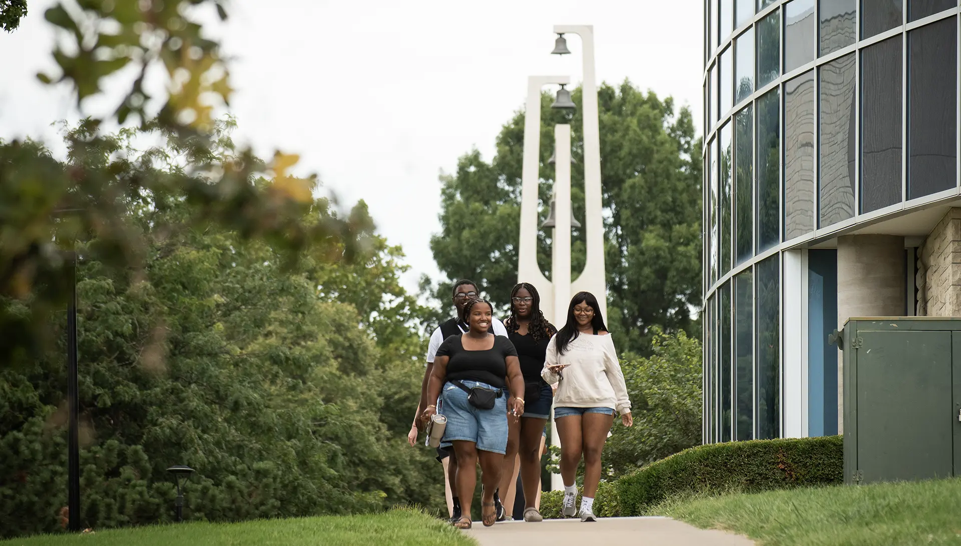 A group of Washburn students smile as they walk on campus with the bell tower behind them.