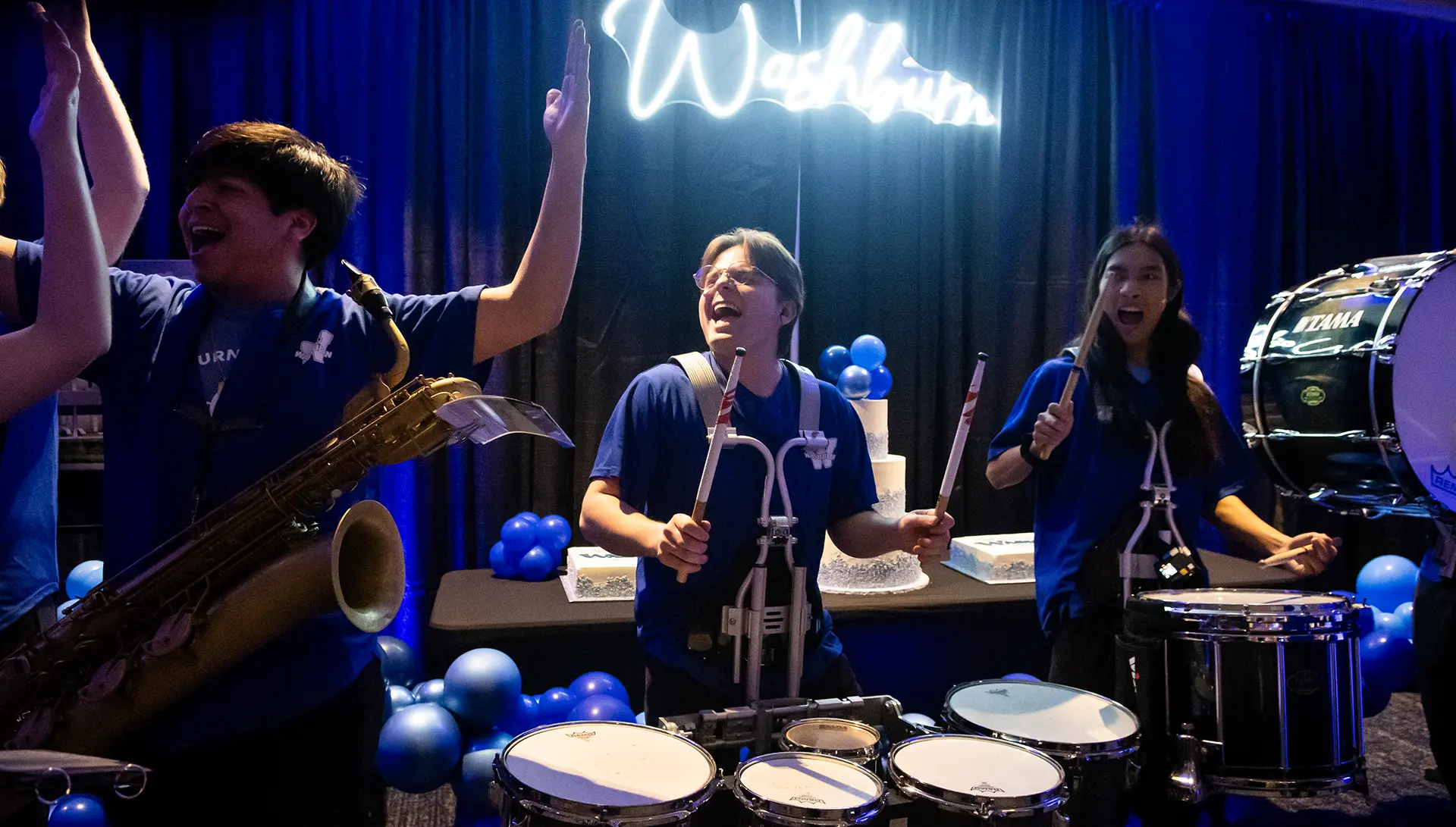 The pep band performs happy birhtday in front of a cake.