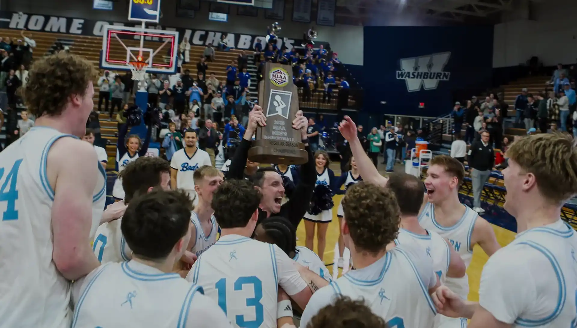 basketball team coach holds up trophy with team cheering on basketball court