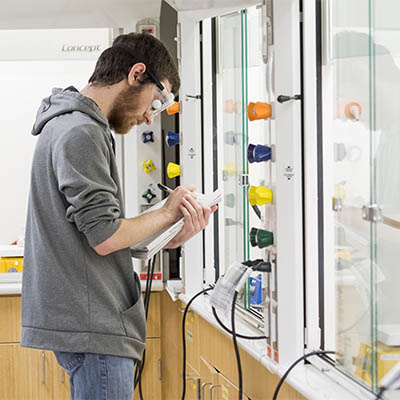 A student takes notes while performing an experiment in a vented lab area.
