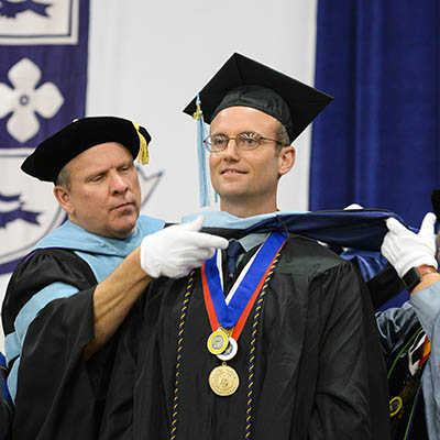 A student receives his cape during graduation.