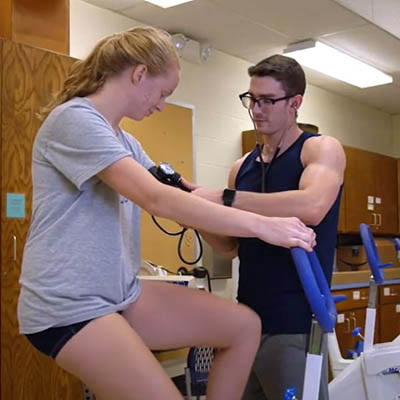 Quinn puts a blood pressure cuff on an athlete who's riding a bike.