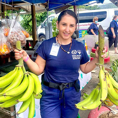 Marquez smiles in her scrubs while holding two bunches of plantains.
