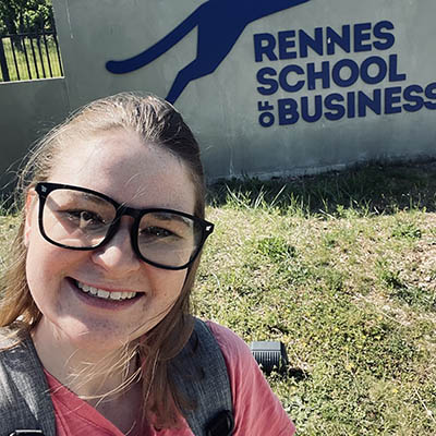 Shelby smiles while standing in front of a Rennes School of Business sign