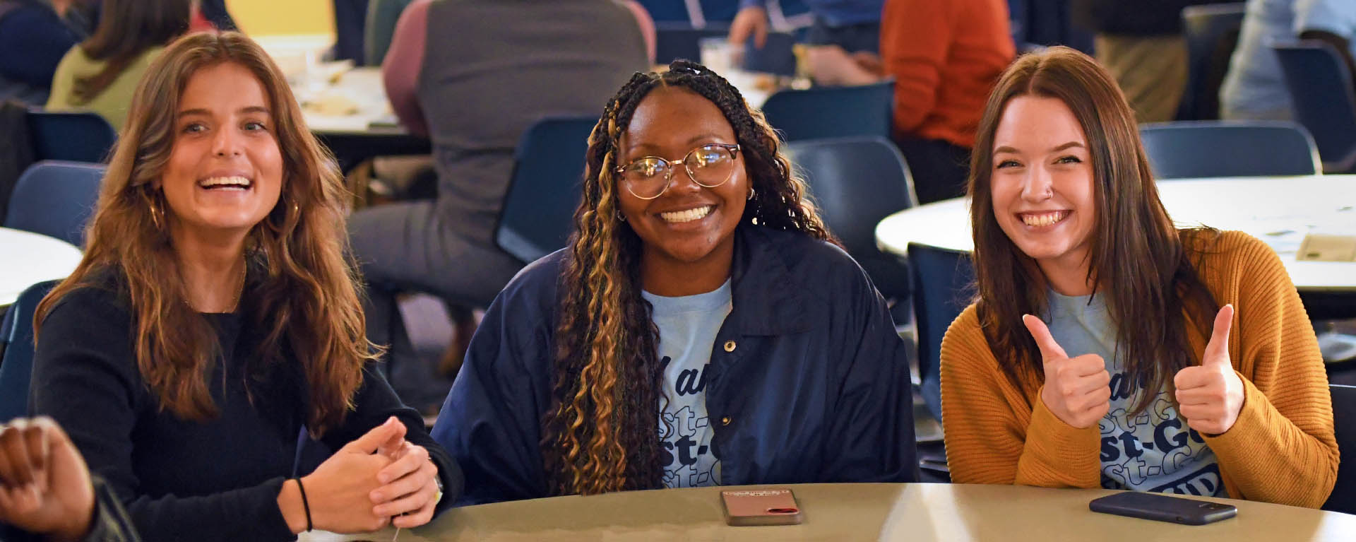 Three Washburn students smile while sitting at a table together at an event.