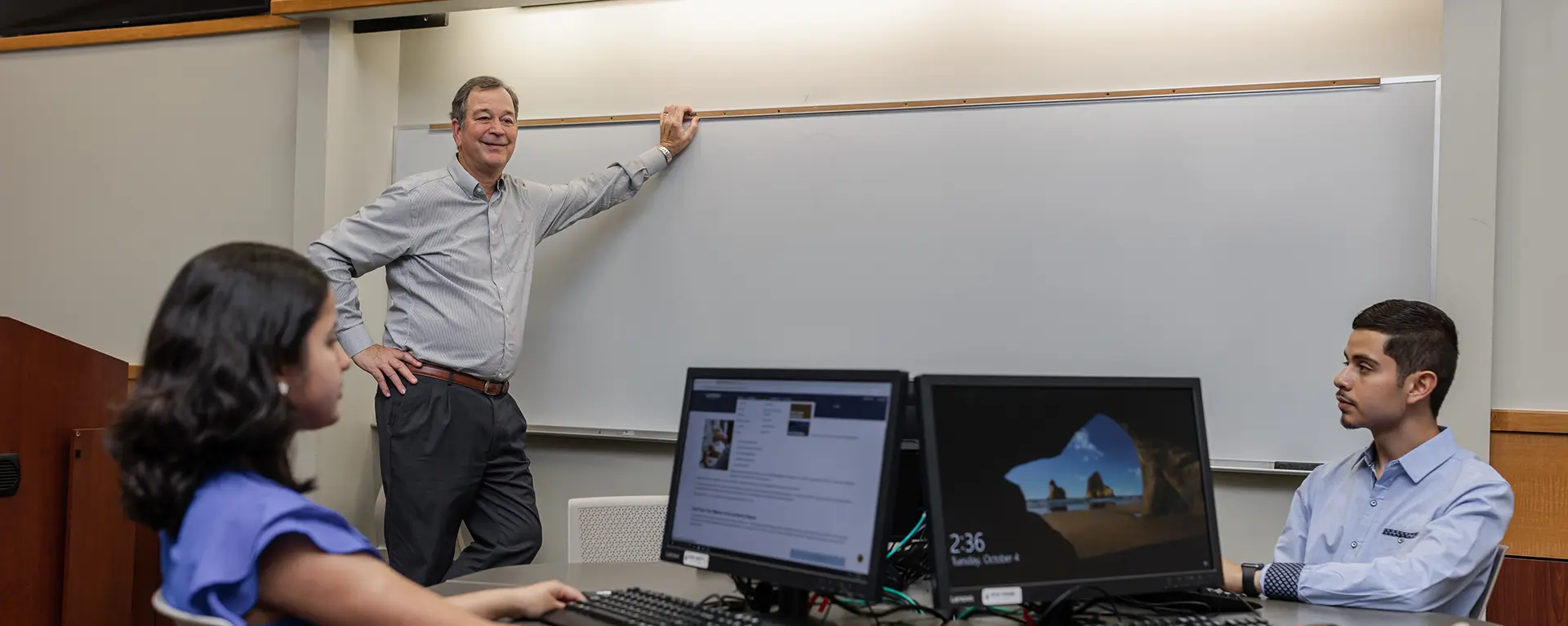 A business professor stands at a white board while talking with students.