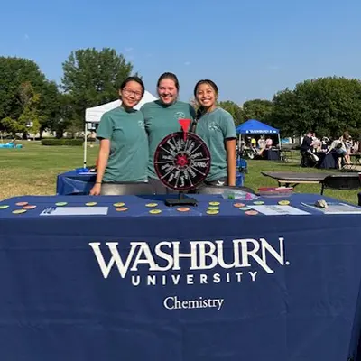 Three chem club members pose for a photo with their table at wufest.