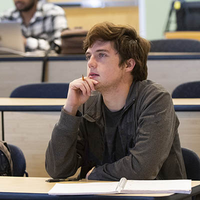 A student looks in thought while taking notes in class.