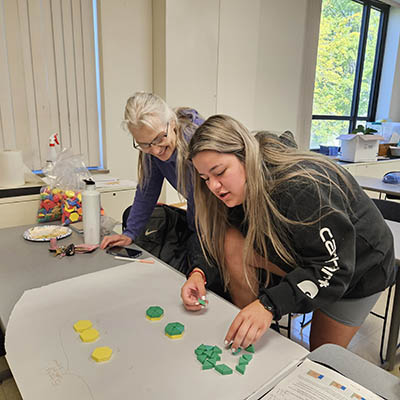 A student works with a math professor on a geometry lesson using tiles.
