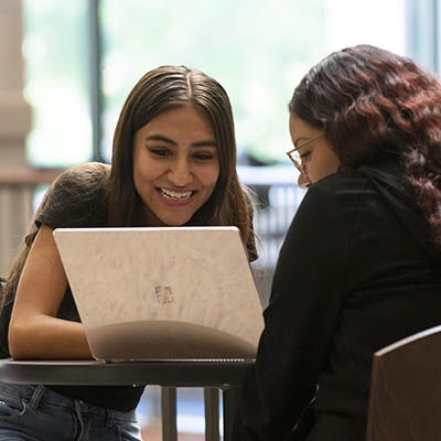 Two students smile while looking at a laptop screen.