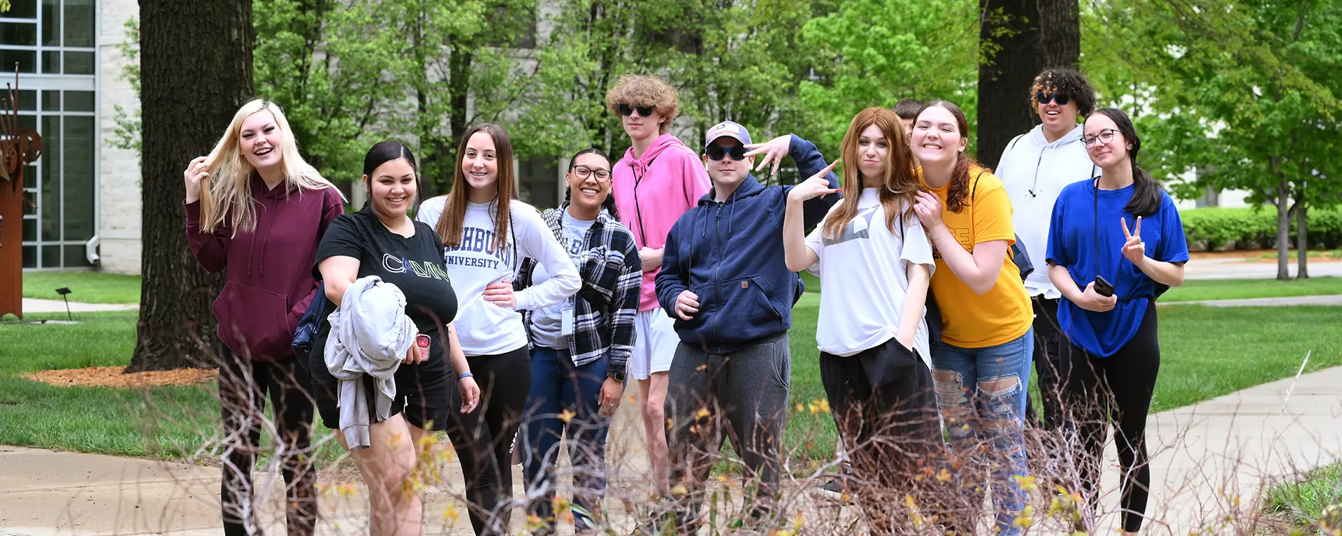 A group of students smile and pose for the camera while walking on campus.