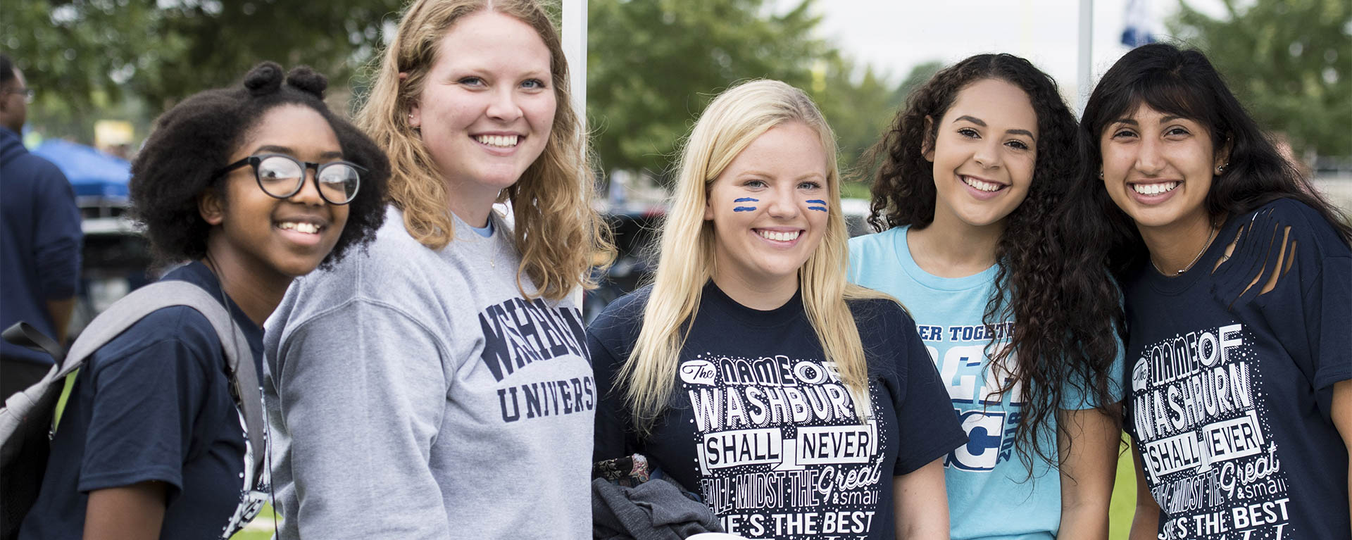 Five students dressed in Washburn blue smile for a photo while tailgating before a football game.