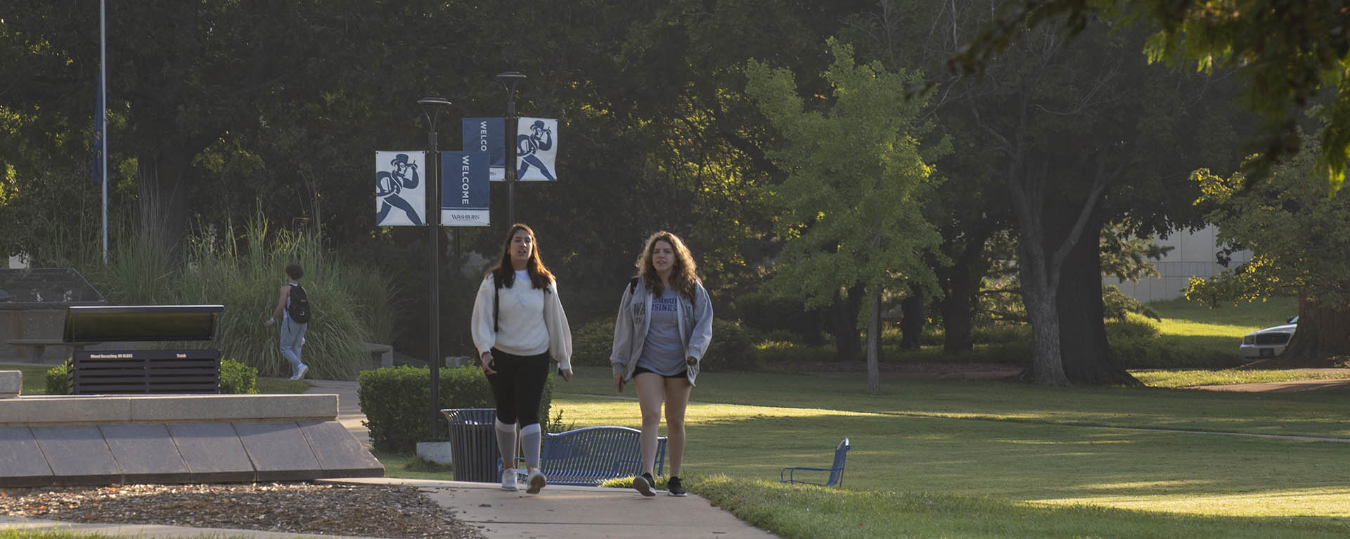 Two students chat while walking to class in soft morning light.